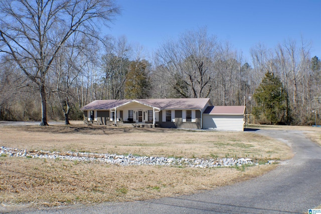 view of front of house with a forest view, covered porch, aphalt driveway, and a front yard