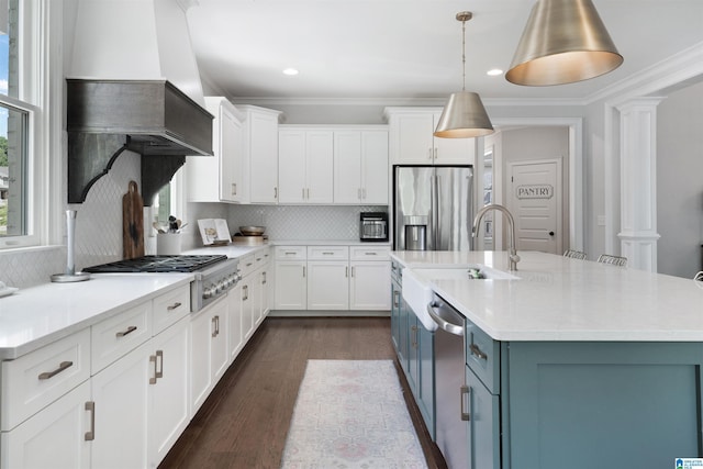 kitchen with custom range hood, decorative columns, appliances with stainless steel finishes, white cabinetry, and a sink