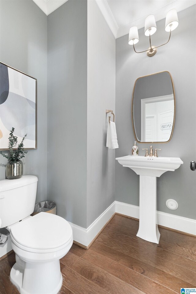 bathroom featuring toilet, a sink, wood finished floors, crown molding, and baseboards