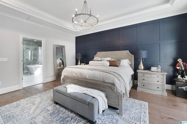 bedroom featuring a tray ceiling, light wood-style flooring, crown molding, a decorative wall, and a notable chandelier