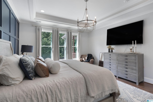 bedroom featuring wood finished floors, baseboards, crown molding, a raised ceiling, and a notable chandelier