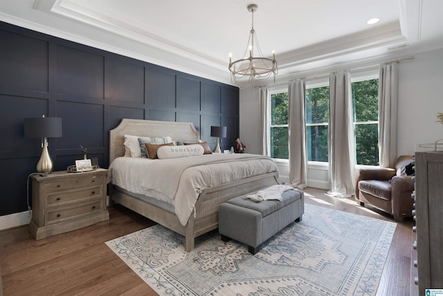 bedroom with a tray ceiling, a decorative wall, a notable chandelier, and wood finished floors