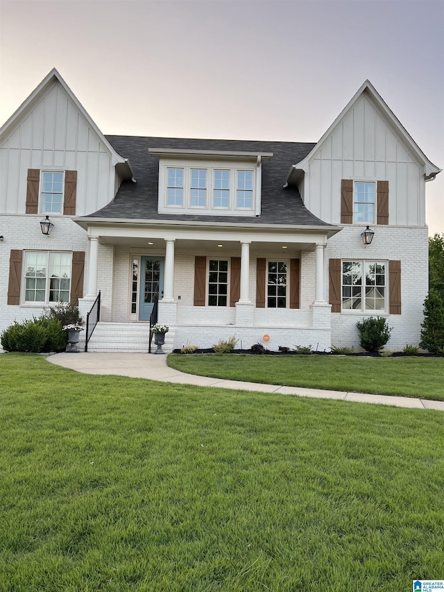 view of front facade featuring a porch, brick siding, board and batten siding, and a front yard