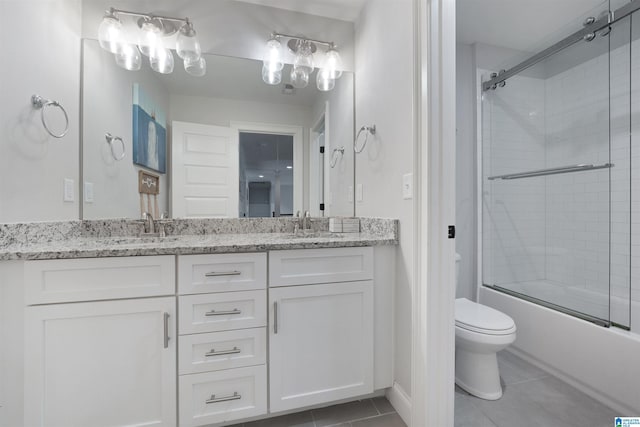 bathroom featuring tile patterned flooring, bath / shower combo with glass door, toilet, double vanity, and a sink