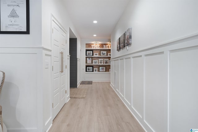 hall featuring recessed lighting, light wood-style floors, wainscoting, and a decorative wall