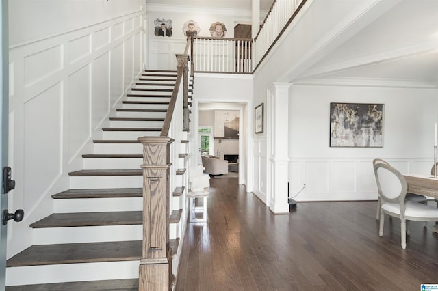 stairway with crown molding, a decorative wall, wood finished floors, and ornate columns