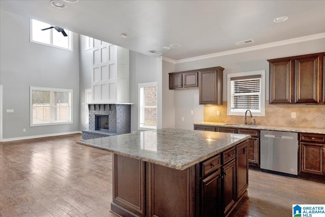 kitchen with visible vents, a fireplace with raised hearth, wood finished floors, stainless steel dishwasher, and a sink