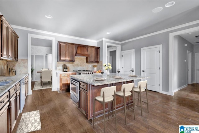 kitchen with appliances with stainless steel finishes, dark wood-type flooring, a kitchen bar, and custom exhaust hood