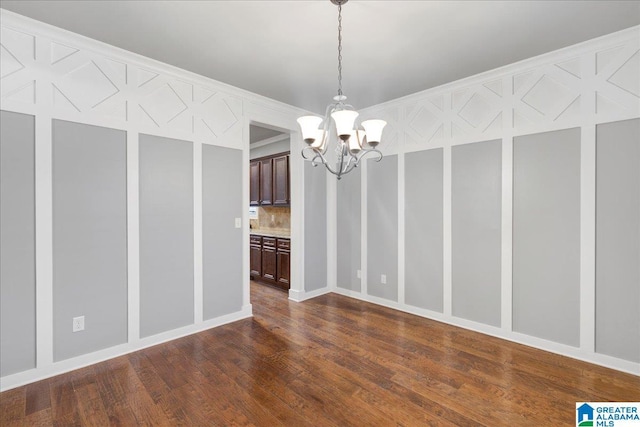 unfurnished dining area featuring dark wood finished floors, a notable chandelier, and a decorative wall