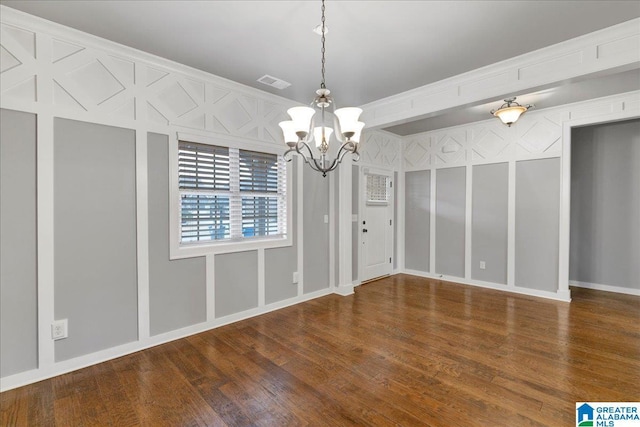 spare room featuring visible vents, a decorative wall, a notable chandelier, and wood finished floors