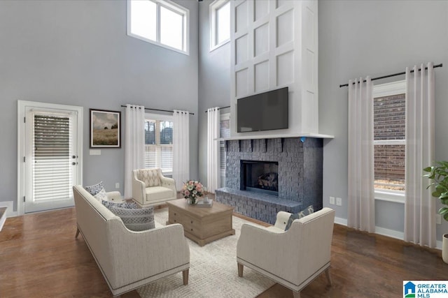 living area featuring a brick fireplace, baseboards, a high ceiling, and wood finished floors