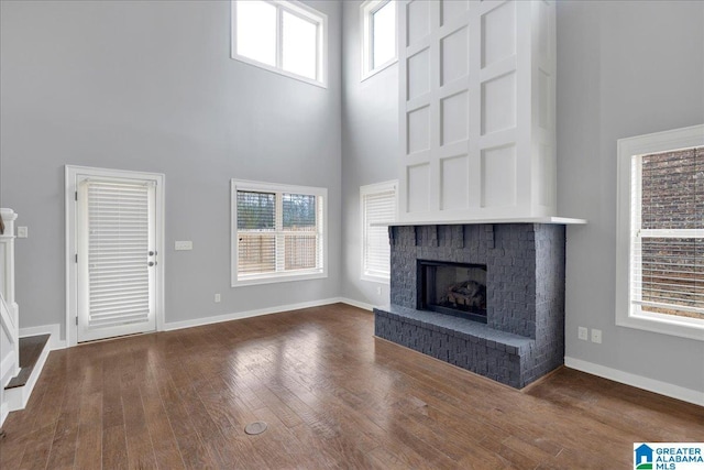 unfurnished living room with a towering ceiling, a fireplace, baseboards, and hardwood / wood-style floors