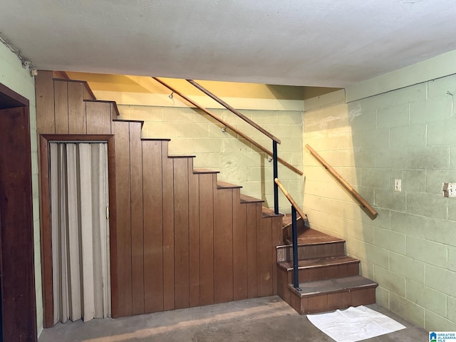 staircase featuring concrete block wall and unfinished concrete flooring