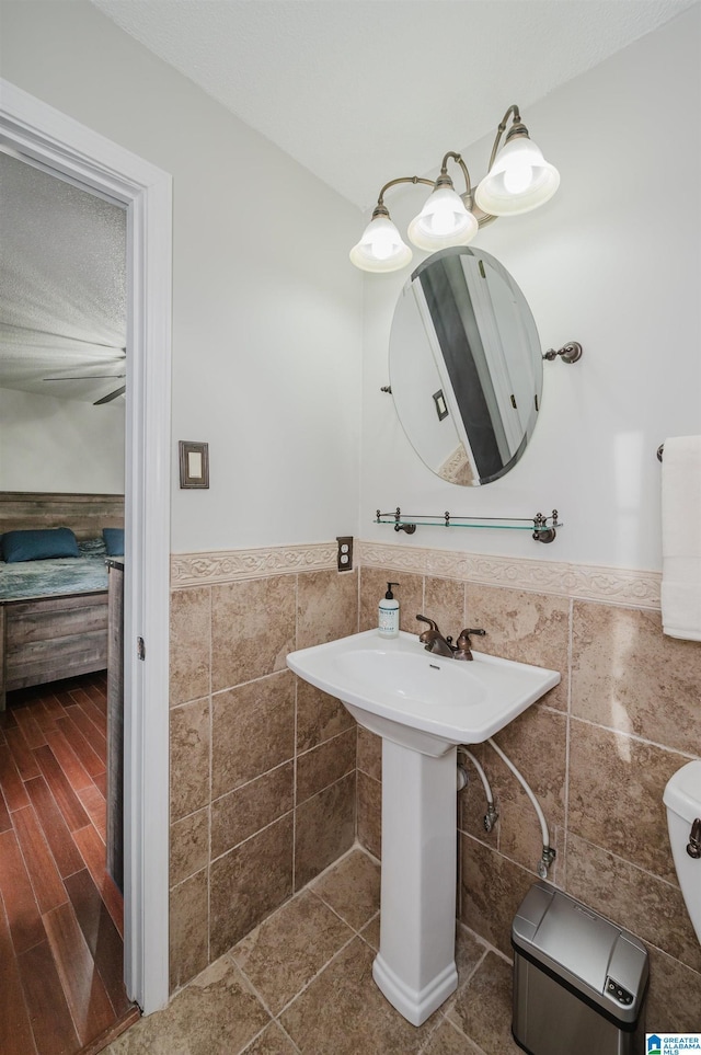 half bath featuring tile walls, toilet, a wainscoted wall, wood finished floors, and a sink