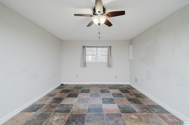 spare room with ceiling fan, stone finish flooring, and baseboards