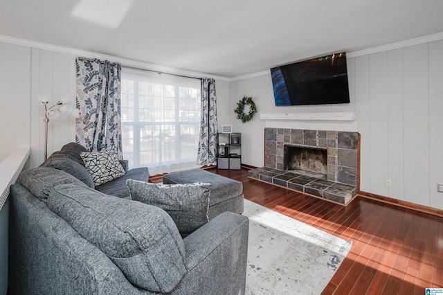 living area with ornamental molding, a fireplace with raised hearth, baseboards, and wood finished floors