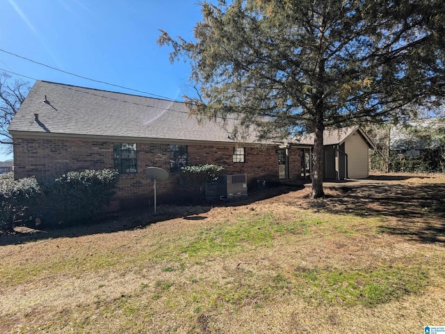 rear view of house featuring a yard, brick siding, roof with shingles, and central AC unit