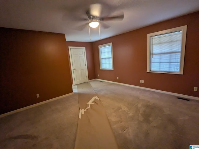 empty room featuring baseboards, ceiling fan, visible vents, and light colored carpet