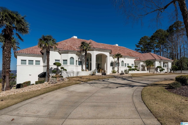 mediterranean / spanish-style home with stucco siding, a tiled roof, and curved driveway