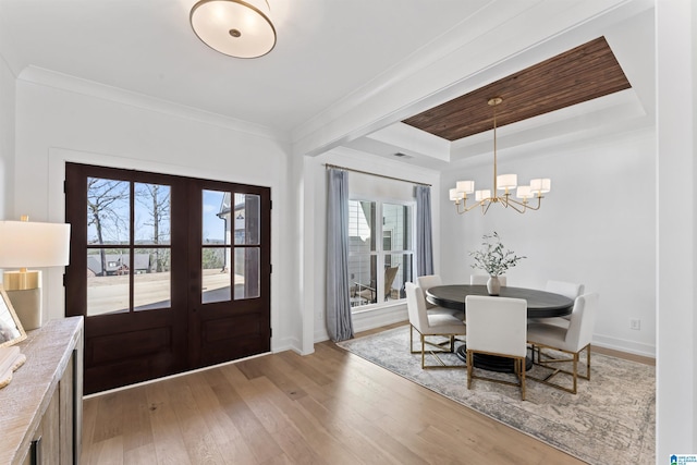 foyer entrance with ornamental molding, a tray ceiling, french doors, and light wood-type flooring