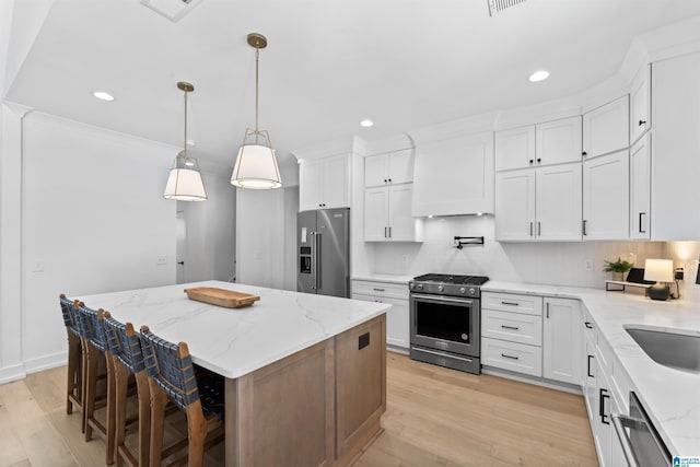 kitchen with stainless steel appliances, white cabinets, premium range hood, and light wood-style floors