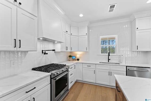 kitchen featuring light wood-style flooring, premium range hood, a sink, white cabinetry, and appliances with stainless steel finishes