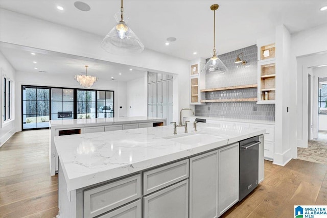 kitchen featuring light wood-type flooring, a center island with sink, a sink, open shelves, and tasteful backsplash