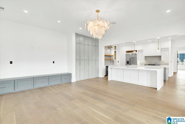 kitchen with tasteful backsplash, light countertops, stainless steel built in fridge, light wood-style floors, and a notable chandelier