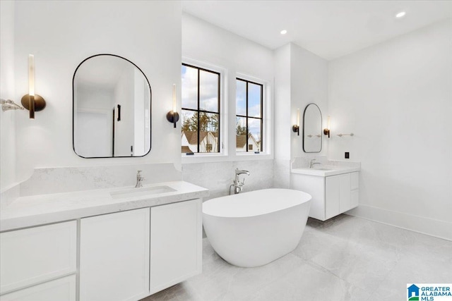 full bathroom featuring a soaking tub, recessed lighting, two vanities, and a sink