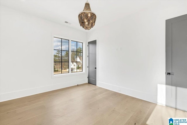 empty room with light wood finished floors, visible vents, and baseboards