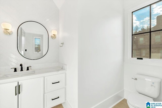 bathroom with a wealth of natural light, baseboards, toilet, and vanity