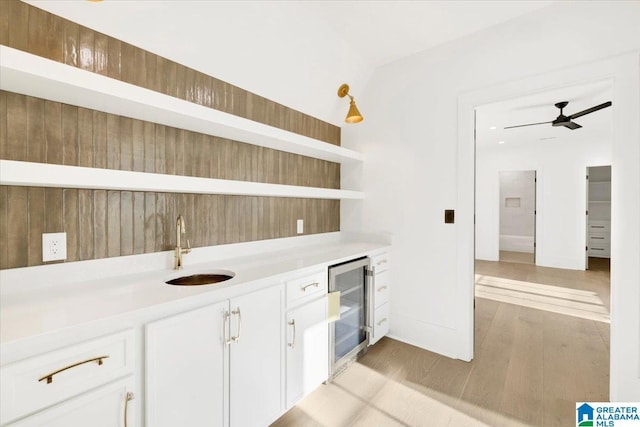 bar with beverage cooler, a sink, light wood-style floors, wet bar, and ceiling fan