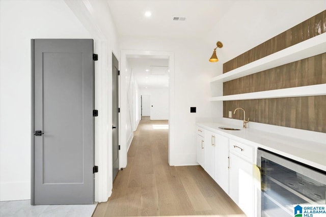 bar featuring baseboards, visible vents, light wood finished floors, a sink, and wine cooler