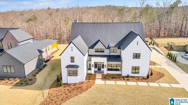 modern farmhouse style home featuring a front yard, a wooded view, and a chimney