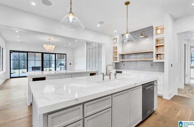 kitchen with light wood-type flooring, an island with sink, gray cabinets, a sink, and open shelves