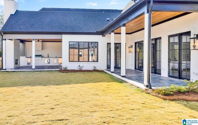 back of property featuring stucco siding, a lawn, a patio, a shingled roof, and a chimney