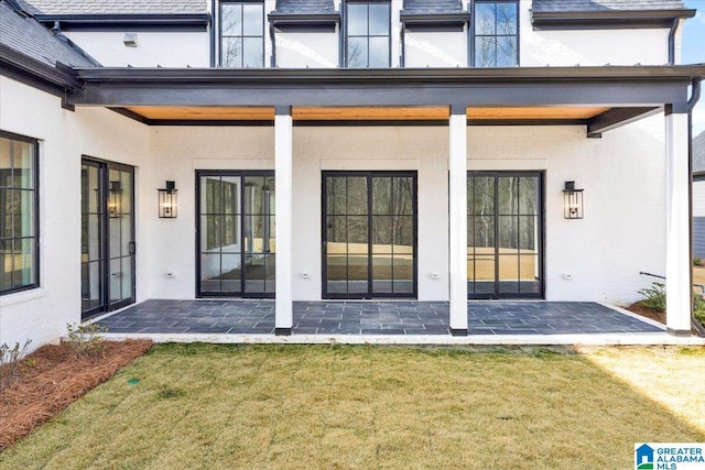 doorway to property featuring stucco siding, a patio, and a yard