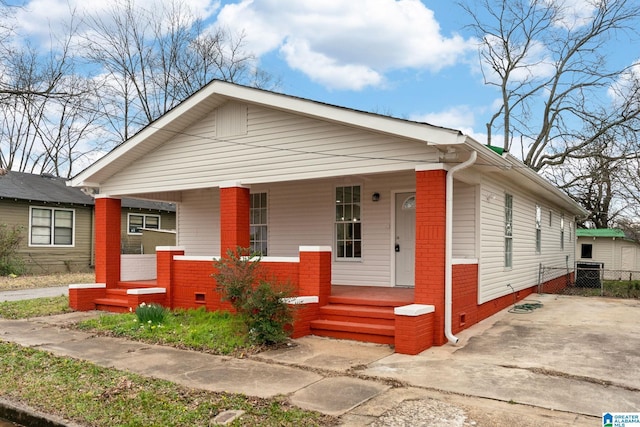 view of front facade with a porch, crawl space, brick siding, and fence