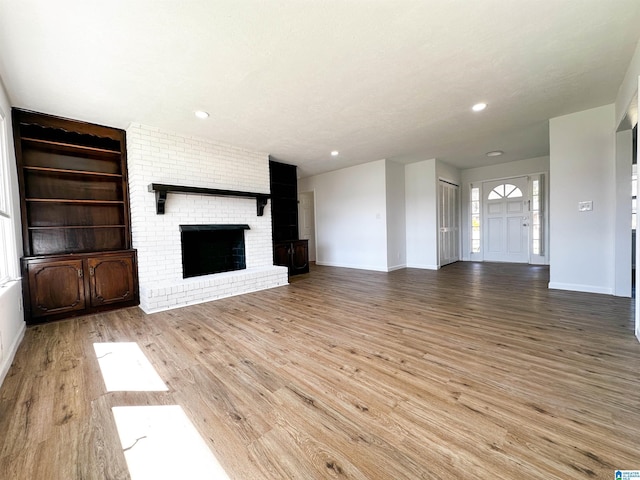 unfurnished living room with built in shelves, wood finished floors, recessed lighting, baseboards, and a brick fireplace