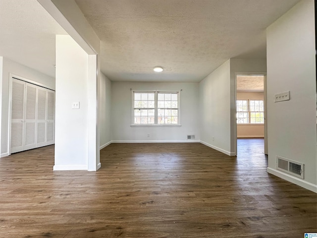 empty room with visible vents, a textured ceiling, and dark wood-type flooring