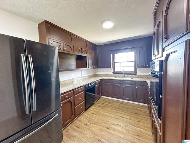 kitchen featuring black appliances, light wood-style flooring, a sink, a textured ceiling, and light countertops