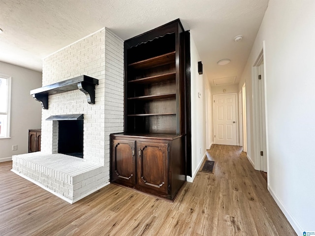 unfurnished living room featuring light wood finished floors, a fireplace, a textured ceiling, and baseboards