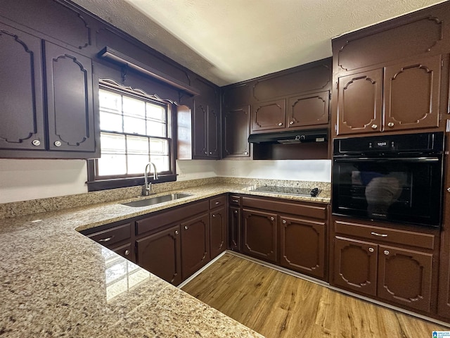 kitchen featuring light wood finished floors, a sink, black appliances, dark brown cabinetry, and under cabinet range hood