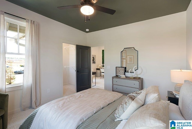 bedroom featuring ceiling fan, baseboards, a walk in closet, and light colored carpet