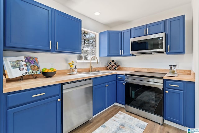 kitchen featuring stainless steel appliances, butcher block countertops, a sink, and blue cabinetry