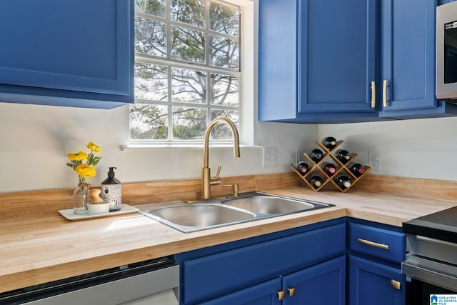 kitchen with dishwasher, butcher block counters, a sink, and blue cabinetry