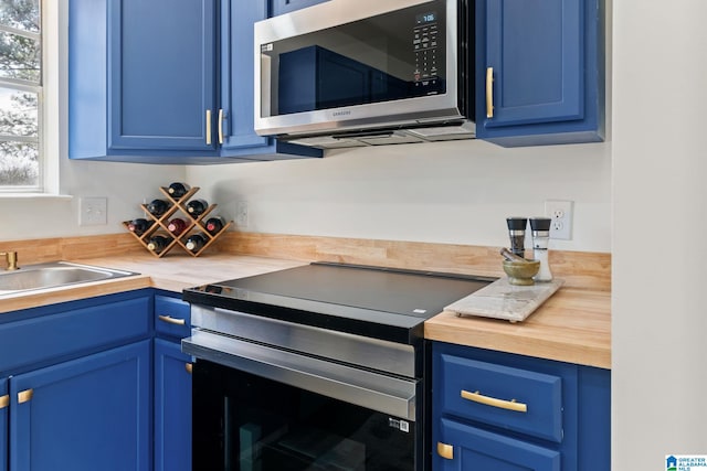 kitchen featuring blue cabinets, butcher block counters, and appliances with stainless steel finishes