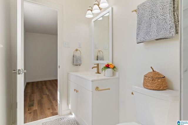 half bath with toilet, wood finished floors, vanity, and baseboards