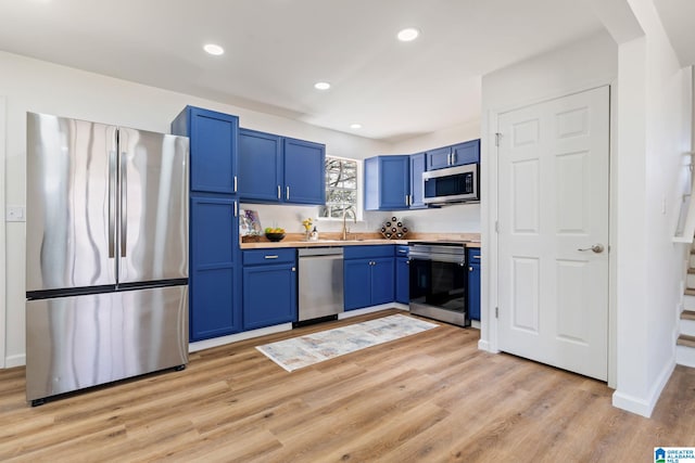 kitchen featuring light wood-style flooring, blue cabinets, a sink, light countertops, and appliances with stainless steel finishes