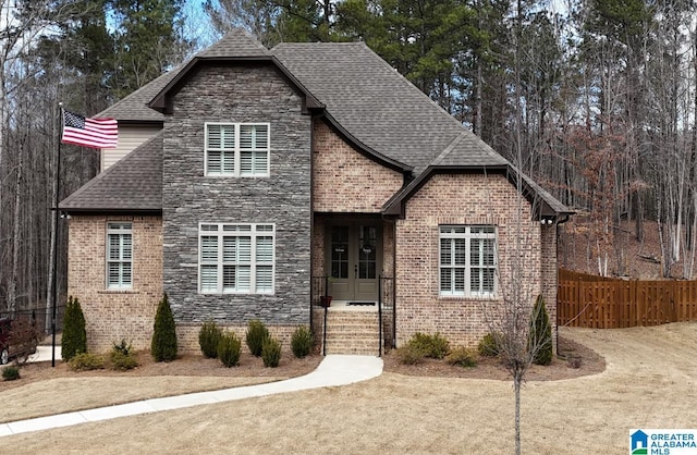 view of front of house featuring fence, a shingled roof, french doors, stone siding, and brick siding